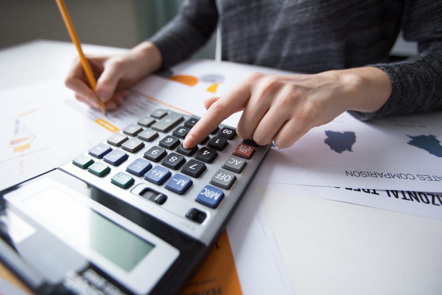 Close-up of female hand counting with calculator, papers all around on table. Businesswoman working with documents